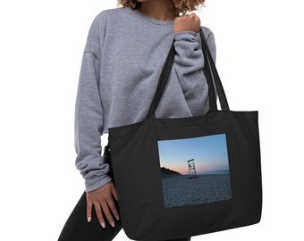 Puede incluir: Una bolsa de tela negra con una silueta de puesto de salvavidas blanco en una playa al atardecer impresa en la parte delantera.