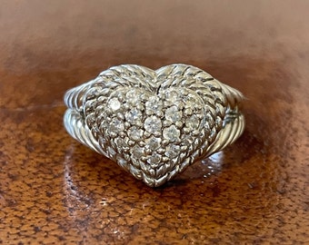 May include: A silver ring with a heart-shaped center set with small diamonds. The band of the ring is braided.