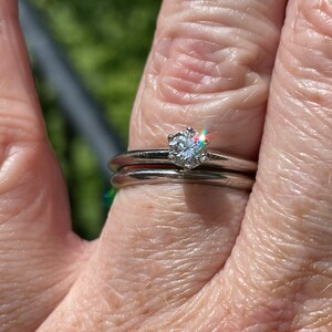 May include: A close-up of a silver wedding band with a single diamond solitaire ring on top. The diamond is sparkling in the sunlight.