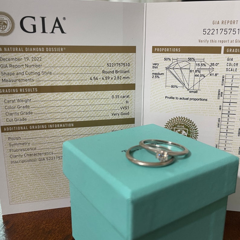 May include: A GIA diamond grading report with a diamond ring in a light blue box. The report shows the diamond is 0.35 carats, H color, VS1 clarity, and Very Good cut. The diamond is round brilliant and measures 4.54-4.59 x 2.82 mm.