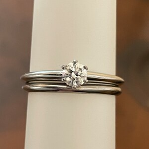 May include: A silver wedding band set with a single round diamond.