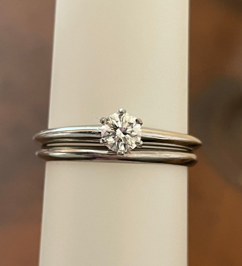 May include: A silver wedding band set with a single round diamond.