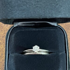 May include: A set of two silver wedding bands with a single diamond solitaire ring in the center. The rings are in a black velvet ring box.