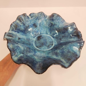 May include: A ceramic bowl with a ruffled, wavy edge and a deep, mottled blue glaze. The interior features a circular base and a textured surface with varying shades of dark and light blue, creating a dynamic, swirling appearance across the piece.