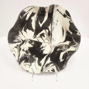 May include: A decorative bowl with a wavy, irregular rim featuring a high-gloss finish. The surface displays a marbled pattern of deep black and creamy white swirls that blend together across the entire interior of the ceramic vessel.