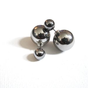 May include: A pair of silver double-sided ball earrings. Each earring has two silver balls, one larger than the other.