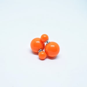 May include: A pair of orange double-sided stud earrings. The earrings have a larger round ball on one side and a smaller round ball on the other side.
