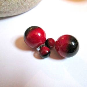 May include: Four red and black earrings with a glossy finish are displayed on a white surface. The earrings are round, with a gradient from red to black. The earrings vary in size, with two larger and two smaller.