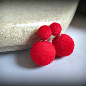 May include: A pair of red velvet earrings with a double ball design. The earrings are on a white surface.