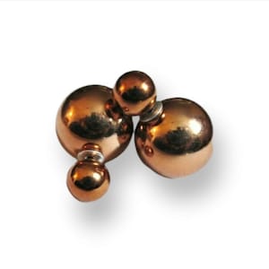 May include: Copper-colored double-sided earrings. Each earring features a large sphere on the front and a smaller sphere on the back, connected by a post. The earrings have a shiny, metallic finish and are set against a white background.