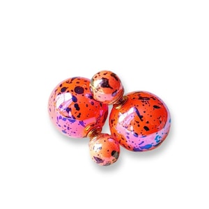 May include: A pair of double-sided earrings with a large orange sphere with black splatter paint and a smaller orange sphere with black splatter paint.