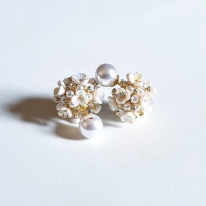 Pode incluir: Um par de brincos de pérolas brancas e flores. Os brincos são feitos de pequenas flores brancas e pérolas, e são presos a um poste dourado.