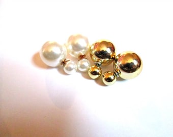 May include: A pair of double-sided earrings with a gold and white pearl design. One earring features a large gold ball and a smaller gold ball, while the other earring features a large white pearl and a smaller white pearl.