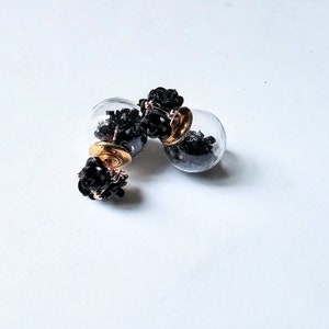 May include: A pair of black and gold double-sided earrings with a cluster of black beads on each side. The earrings are made of glass and metal.