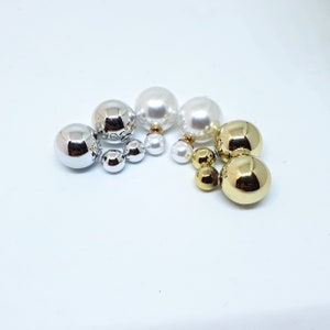 Può includere: Un set di tre paia di orecchini a doppia faccia. Ogni paio presenta una grande sfera perlata da un lato e una sfera più piccola dall'altro. Gli orecchini sono disponibili in argento, oro e bianco.