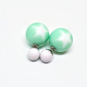 May include: A pair of double-sided earrings with a mint green ball on one side and a white ball on the other. The mint green ball has a white star design.