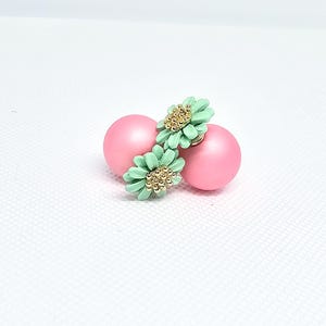 May include: A pair of pink and green double-sided earrings with a flower design. The earrings are made of plastic and have a shiny finish.