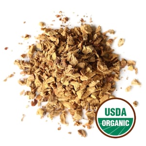 May include: A pile of chopped, dried ginger pieces, in shades of tan and brown, against a white background. A USDA Organic seal is visible in the lower right corner. The ginger appears to be ready for cooking or tea.