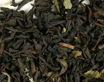 May include: Close-up of loose leaf black tea with green leaf pieces. The tea is dark brown and black in color.