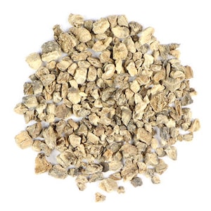 Pode incluir: Um close-up de um monte de pedaços de raiz de angélica seca, de cor castanho claro e forma irregular.