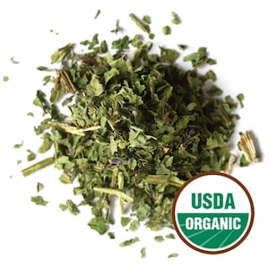 Könnte beinhalten: Ein Haufen getrockneter, gehackter grüner Kräuter, möglicherweise für kulinarische oder medizinische Zwecke, vor weißem Hintergrund. Das Bild enthält ein USDA Organic-Siegel, das die Zertifizierung des Produkts anzeigt.