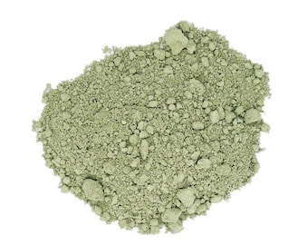 May include: A pile of light green powder with a granular texture, set against a white background. The powder appears to be finely ground, with small, irregular clumps scattered throughout. The color is a muted, earthy green.