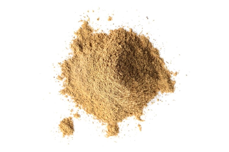 May include: A pile of light brown powder against a white background. The powder has a fine texture and appears to be a spice or herb. The image is a top-down view, with the powder taking up most of the frame.