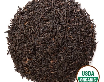 May include: A close-up of a pile of loose leaf tea. The tea leaves are dark brown and appear to be dried. A green and white USDA Organic seal is in the lower right corner. The tea is likely for brewing.