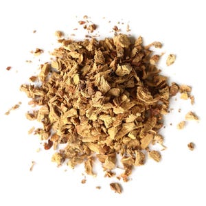 May include: A pile of dried, chopped ginger pieces, in shades of light and medium brown, against a white background. The ginger pieces are irregularly shaped and textured, suggesting a natural, unprocessed product. The image is a top-down view.