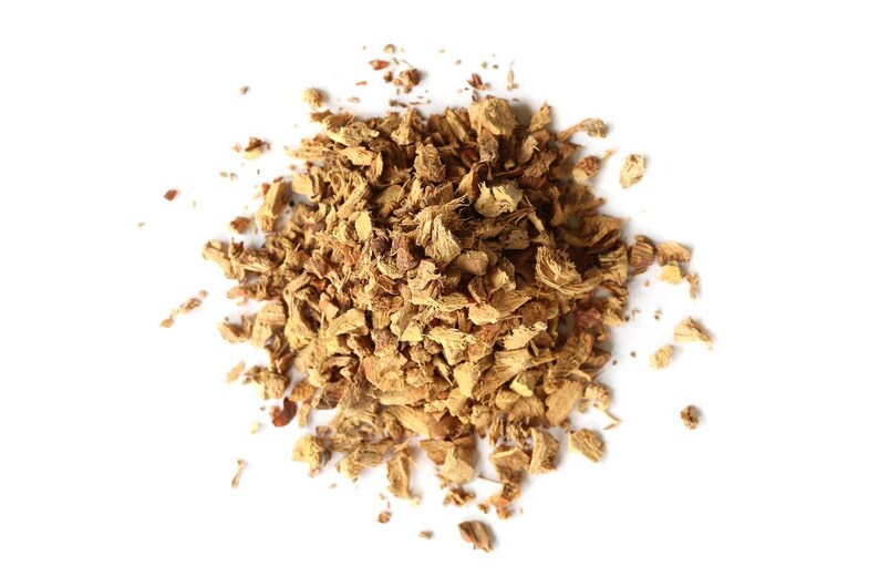 May include: A pile of dried, chopped ginger pieces, in shades of light and medium brown, against a white background. The ginger pieces are irregularly shaped and textured, suggesting a natural, unprocessed product. The image is a top-down view.