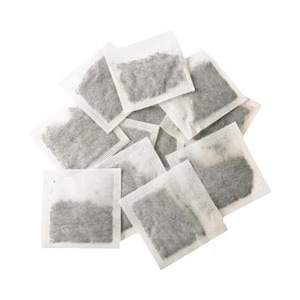 May include: A collection of square, white tea bags filled with loose tea leaves. The tea bags are arranged in a slightly overlapping pattern, with the tea leaves visible through the translucent paper.