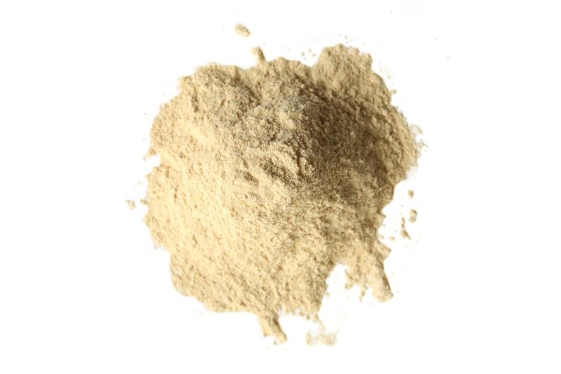 May include: A close-up of a pile of light brown powder on a white background. The powder has a fine texture and appears to be a natural substance. The powder is scattered in a circular shape.