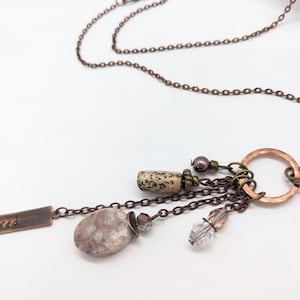 May include: A copper chain necklace with a charm featuring a small stone, a crystal, and a metal tag that says "Love".