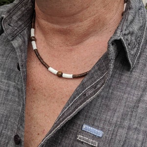 May include: A close-up of a man wearing a gray denim shirt with a brown and white beaded necklace.