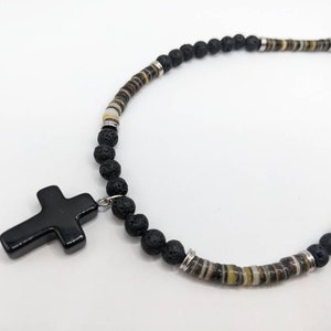 May include: A black lava rock beaded necklace with a black cross pendant. The necklace has silver accents and brown and white striped beads.