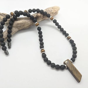 May include: A black lava stone necklace with a rectangular pendant. The necklace features tiger eye stone accents and silver-toned metal spacers. The pendant is a light brown color.