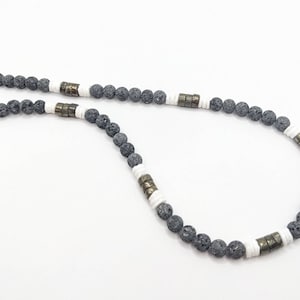 May include: A gray lava rock beaded necklace with white and gold accents. The necklace is made of natural lava rock beads and features a simple design.