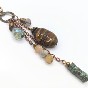 May include: A copper chain necklace with a variety of beads and charms, including a tiger's eye stone, a crystal bead, and a green stone bead.