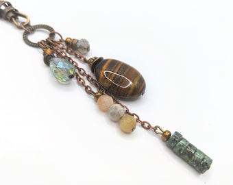May include: A copper chain necklace with a variety of beads and charms, including a tiger's eye stone, a crystal bead, and a green stone bead.