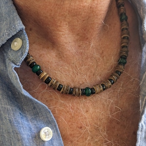 May include: A close-up of a wooden and green bead necklace worn by a person. The necklace is made of brown wooden beads with black accents and green beads.