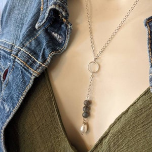 May include: A silver chain necklace with a circle pendant and a single pearl charm. The necklace also features three dark grey beads.