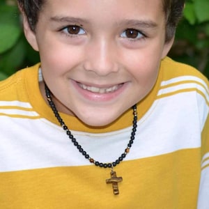 May include: A young boy wearing a yellow and white striped shirt with a black beaded necklace and a wooden cross pendant.