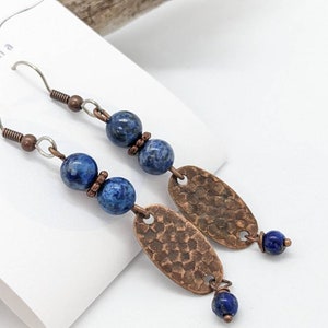 May include: A pair of dangle earrings with blue lapis lazuli beads and hammered copper oval charms. The earrings have silver hooks.