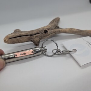 May include: A silver-toned metal bullet-shaped keyring featuring a small rectangular copper-coloured plate engraved with the name Zeb. The keyring includes a circular ring and a lobster clasp, attached to a white tag with the text handmade with aloha.
