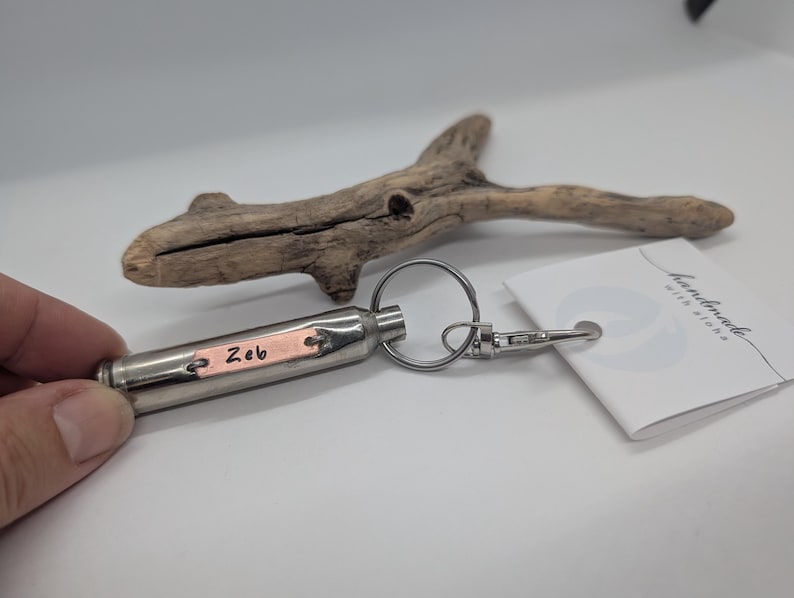 May include: A silver-toned metal bullet-shaped keyring featuring a small rectangular copper-coloured plate engraved with the name Zeb. The keyring includes a circular ring and a lobster clasp, attached to a white tag with the text handmade with aloha.