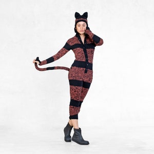 May include: A woman wearing a black and red striped cat costume with a black cat ears headband. The costume has a long tail and a zipper down the front.