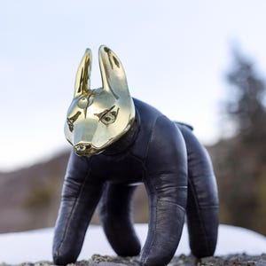 May include: A decorative sculpture of a stylized animal with a gold-colored head and black body. The sculpture is posed on a rock, with a blurred natural background.