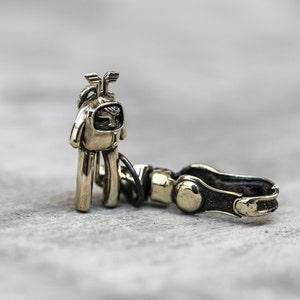 May include: A gold-colored metal keychain featuring a small astronaut figure with a helmet and a larger, round, metal ring.