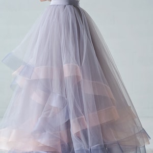 May include: A layered tulle skirt in shades of gray and pink. The skirt has a wide waistband and a flowing silhouette.