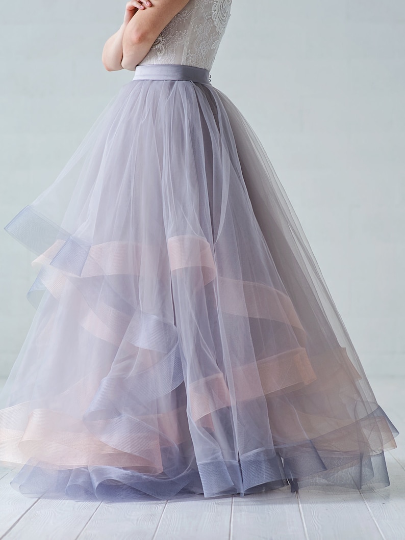 May include: A layered tulle skirt in shades of gray and pink. The skirt has a wide waistband and a flowing silhouette.